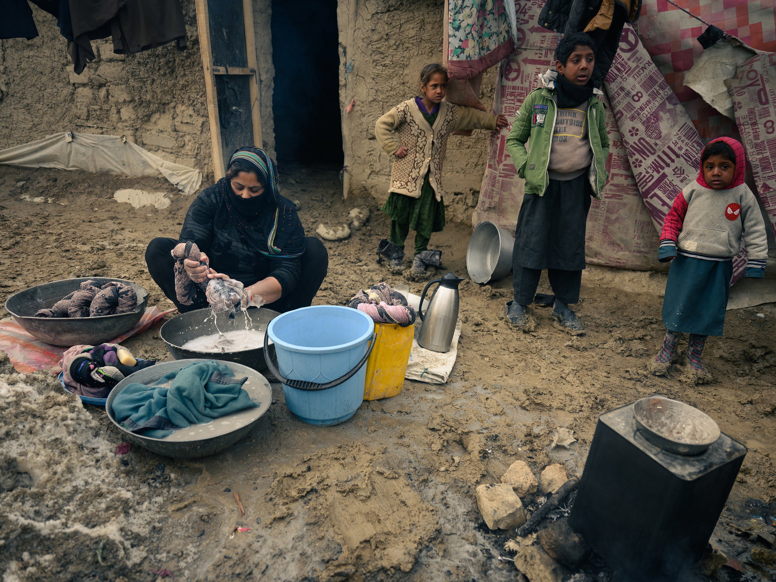 Farzana, 32, washes clothes in front of her mud-walled home in a camp for displaced people on the outskirts of Kabul