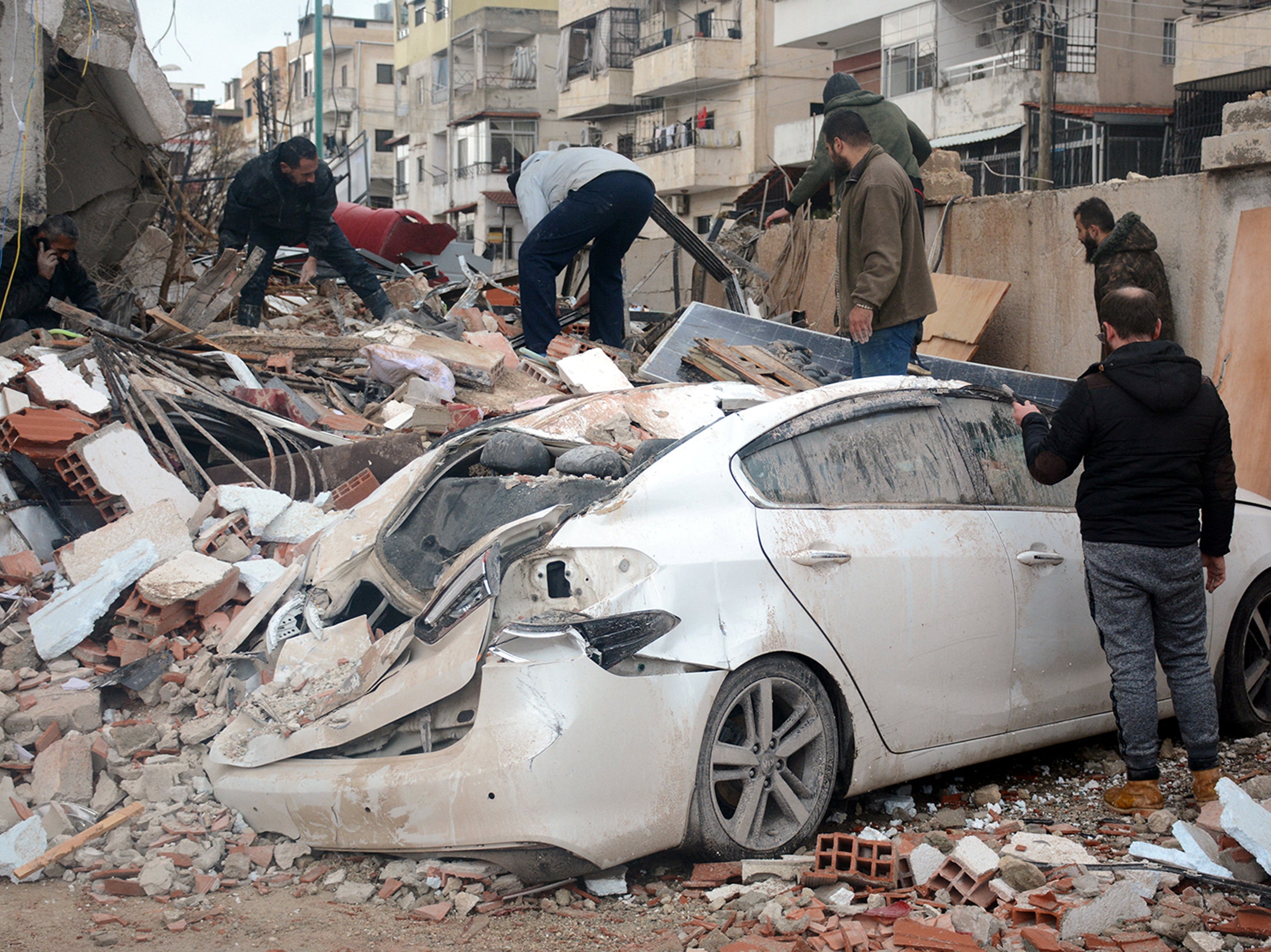 Rescuers search for survivors at the site of a collapsed building, following an earthquake, in Latakia, Syria