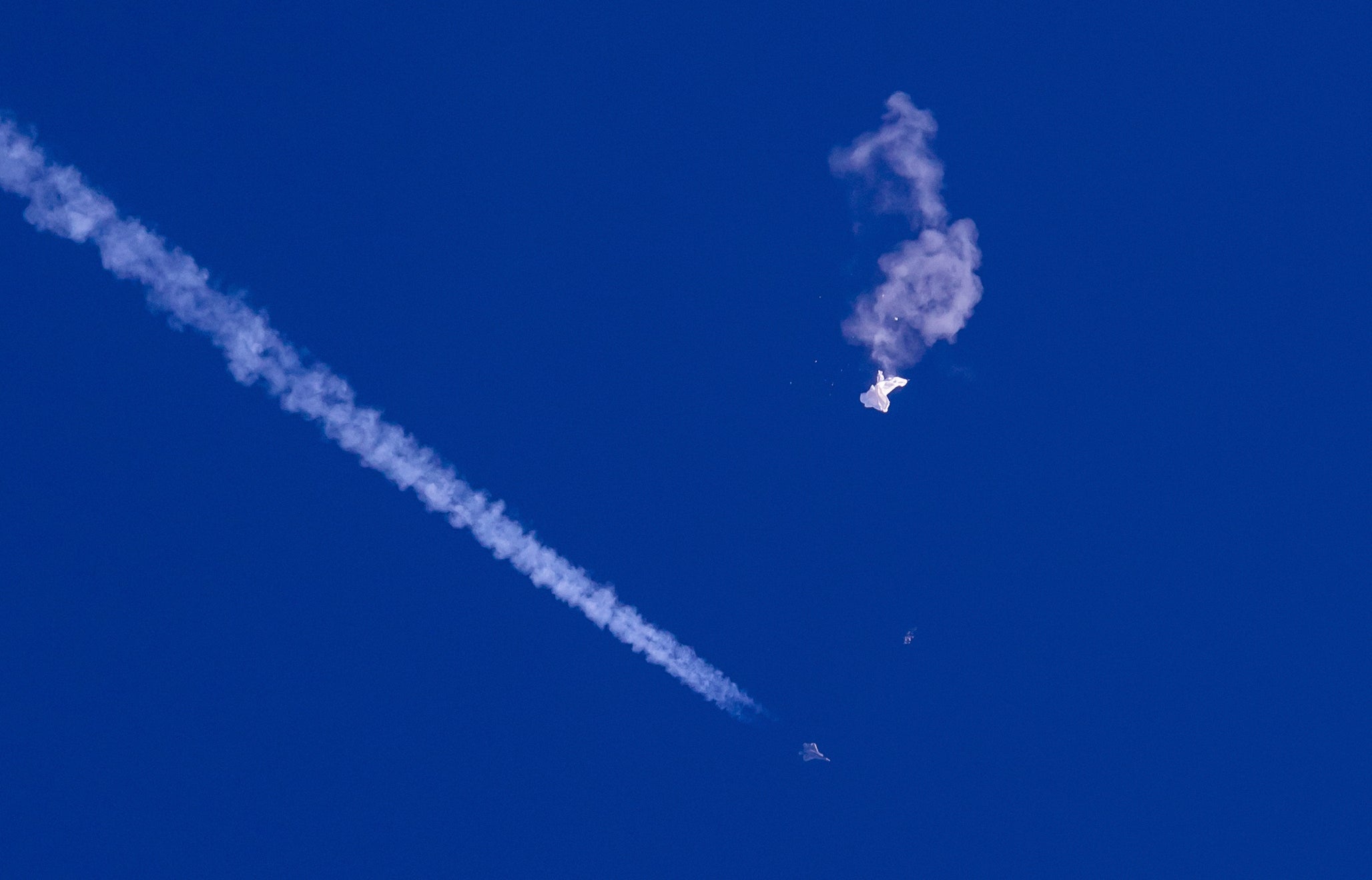 In this photo provided by Chad Fish, the remnants of a large balloon drift above the Atlantic Ocean, just off the coast of South Carolina, with a fighter jet and its contrail seen below it on 4 February