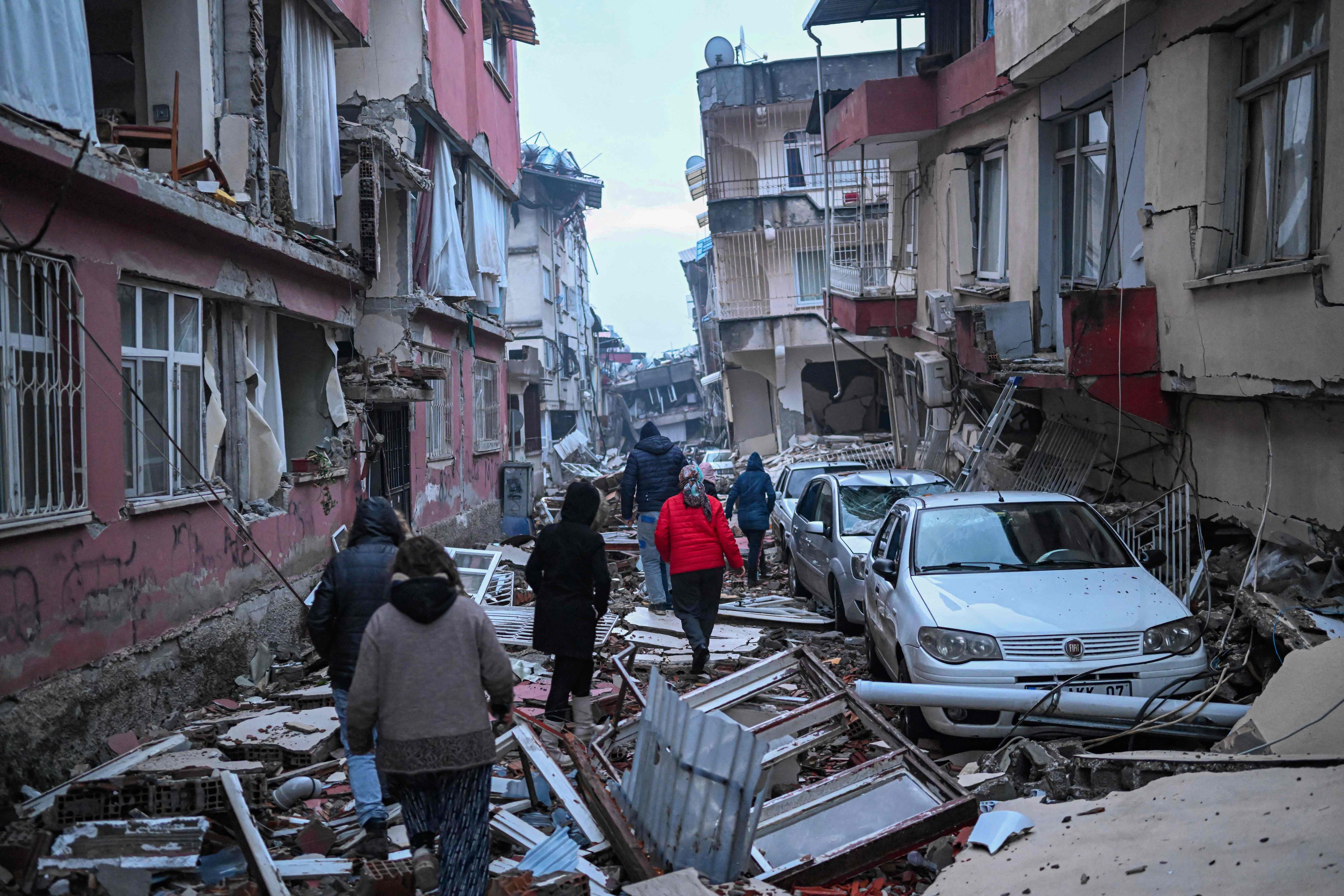 People walk along a street strewn with debris as they look for relatives in Hatay, southeastern Turkey