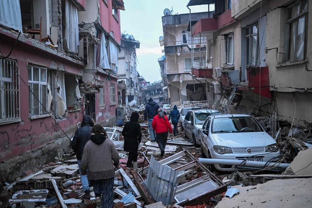<p>People walk along a street strewn with debris as they look for relatives in Hatay, southeastern Turkey</p>