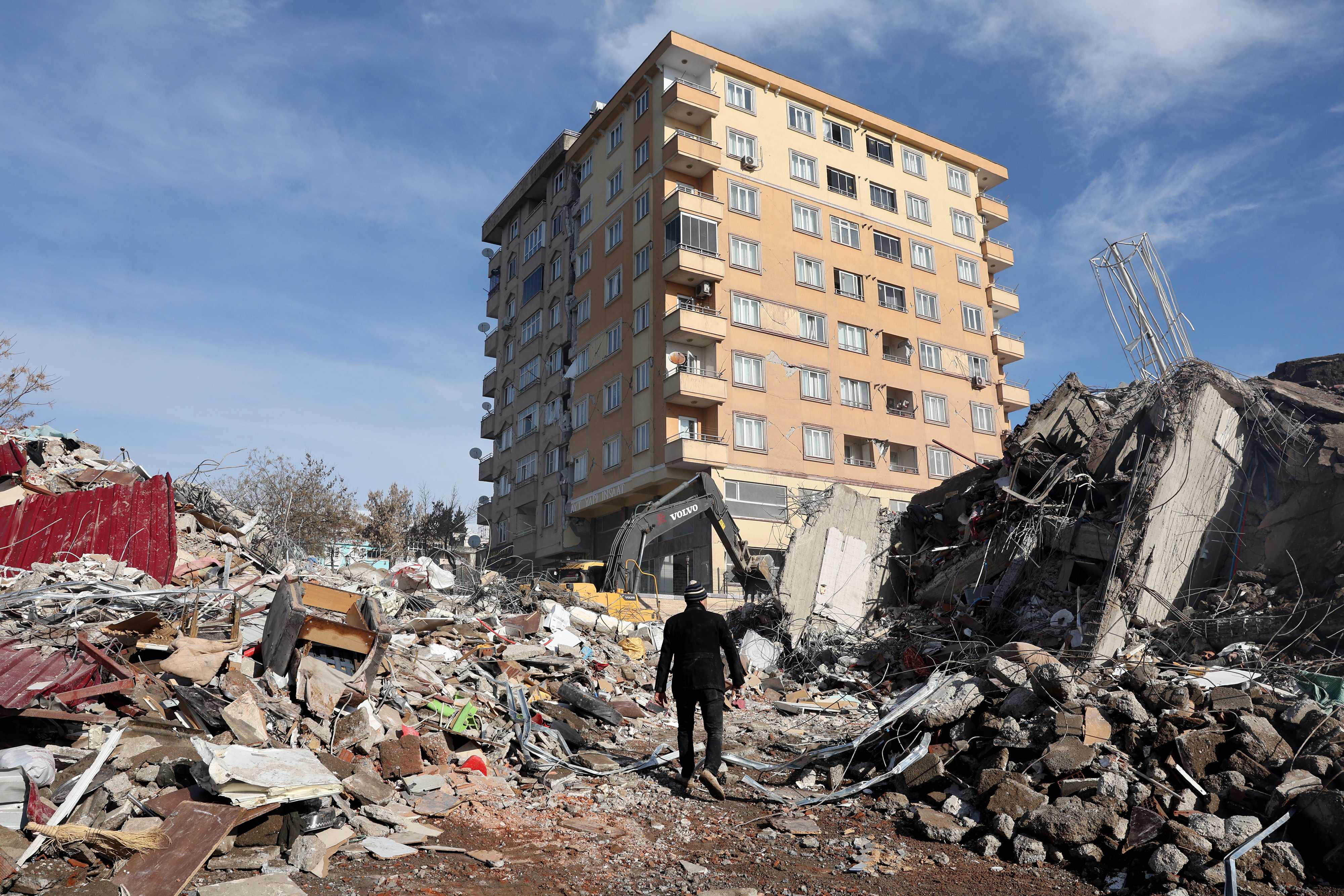 A man walks across the rubble of collapsed building towards a building still standing in Kahramanmaras
