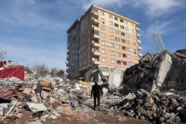 <p>A man walks across the rubble of collapsed building towards a building still standing in Kahramanmaras</p>