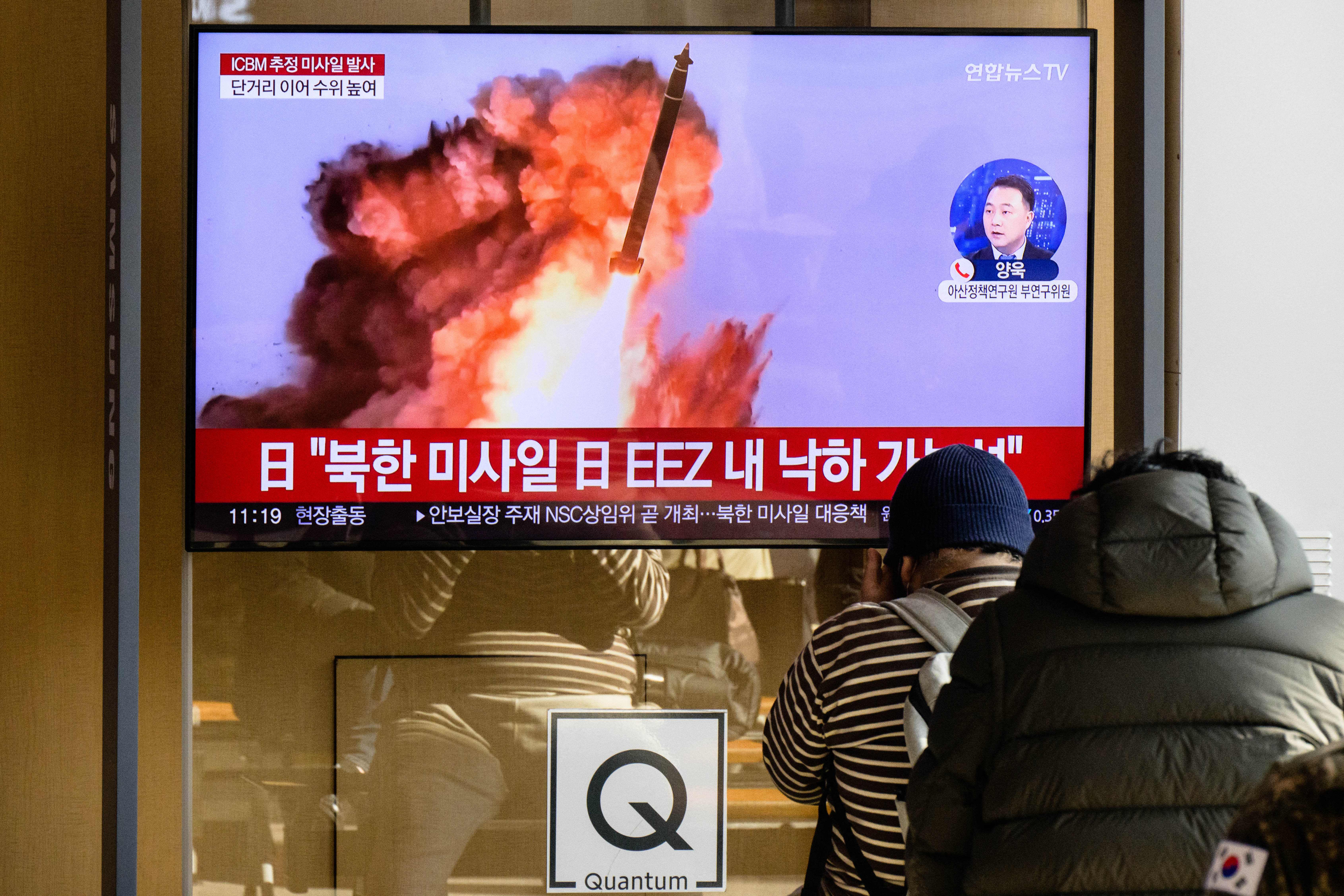 People sit near a television showing a news broadcast with file footage of a North Korean missile test