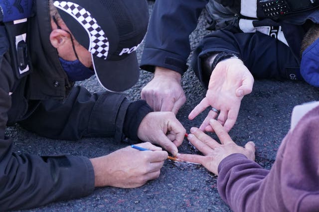 Police officers remove a protester glued to the road at an Insulate Britain roadblock near to the South Mimms roundabout at the junction of the M25 and A1 (Ian West/PA)