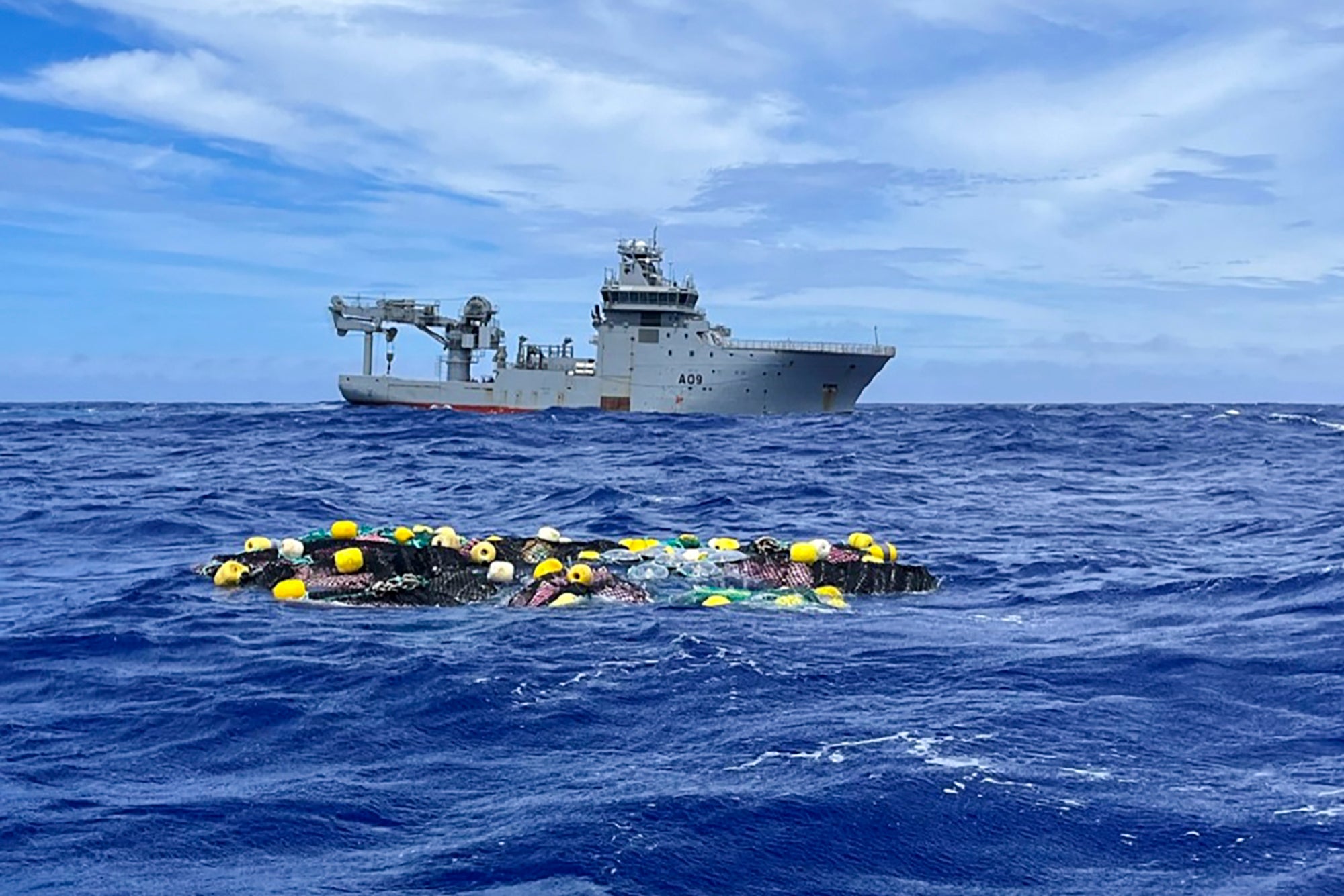 The shipment of cocaine floats on the surface of the Pacific Ocean with the Royal New Zealand Navy vessel HMNZS Manawanui behind