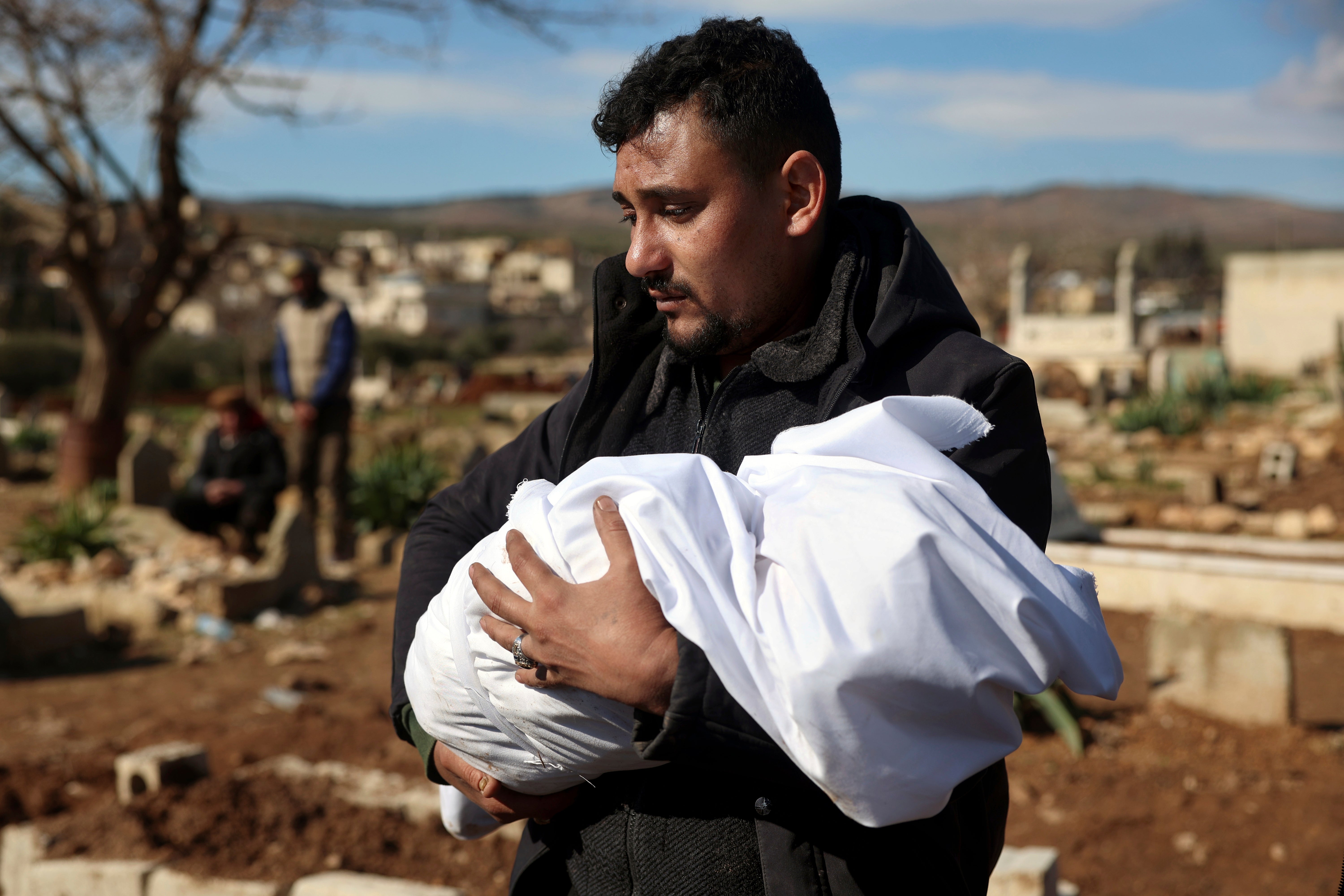A man carries the body of a family member who died in a devastating earthquake that rocked Syria and Turkey at a cemeter