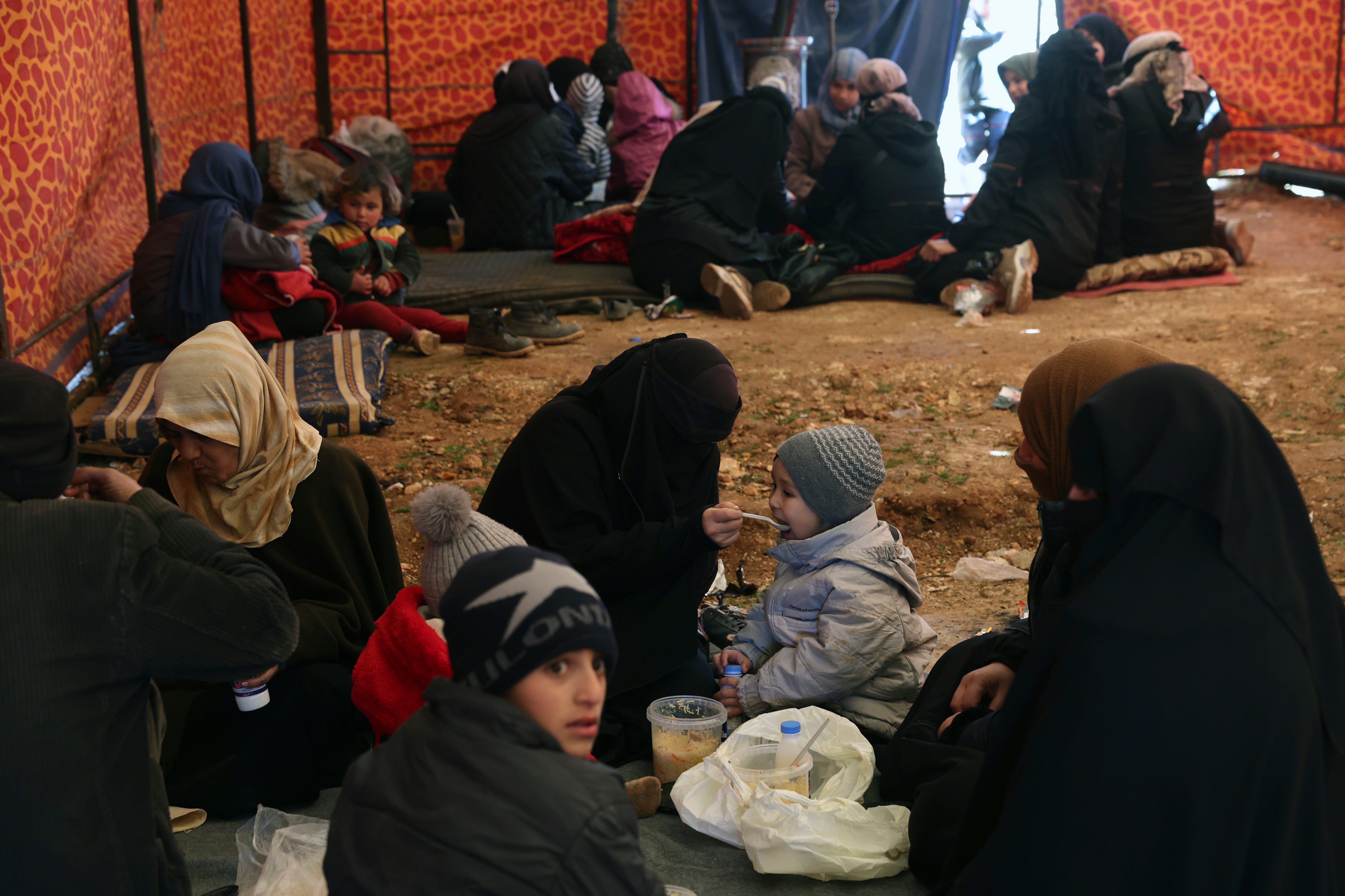 Families who lost their homes in a devastating earthquake in Syria sit inside a tent that an NGO set up