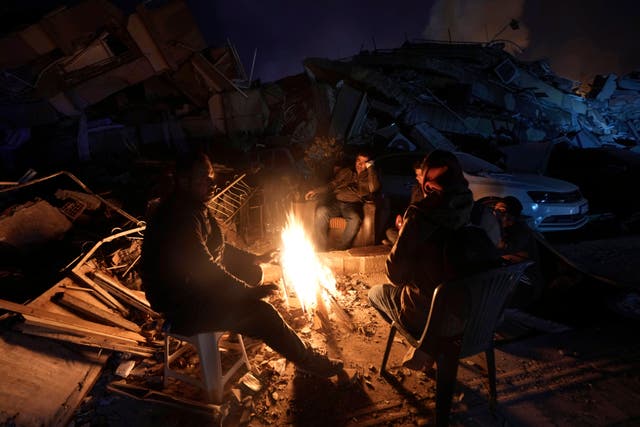 <p>People warm up with fire in front of destroyed buildings in Antakya, southern Turkey, Wednesday, Feb. 8, 2023</p>