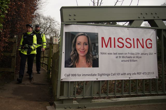 <p>Police officers walk towards a missing person appeal poster for Nicola Bulley on a bridge</p>