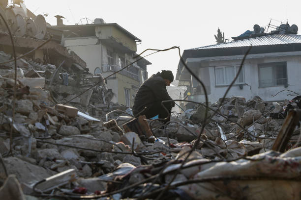 A man sits on top of a collapsed buinding on 13 February 2023 in Hatay, Turkey