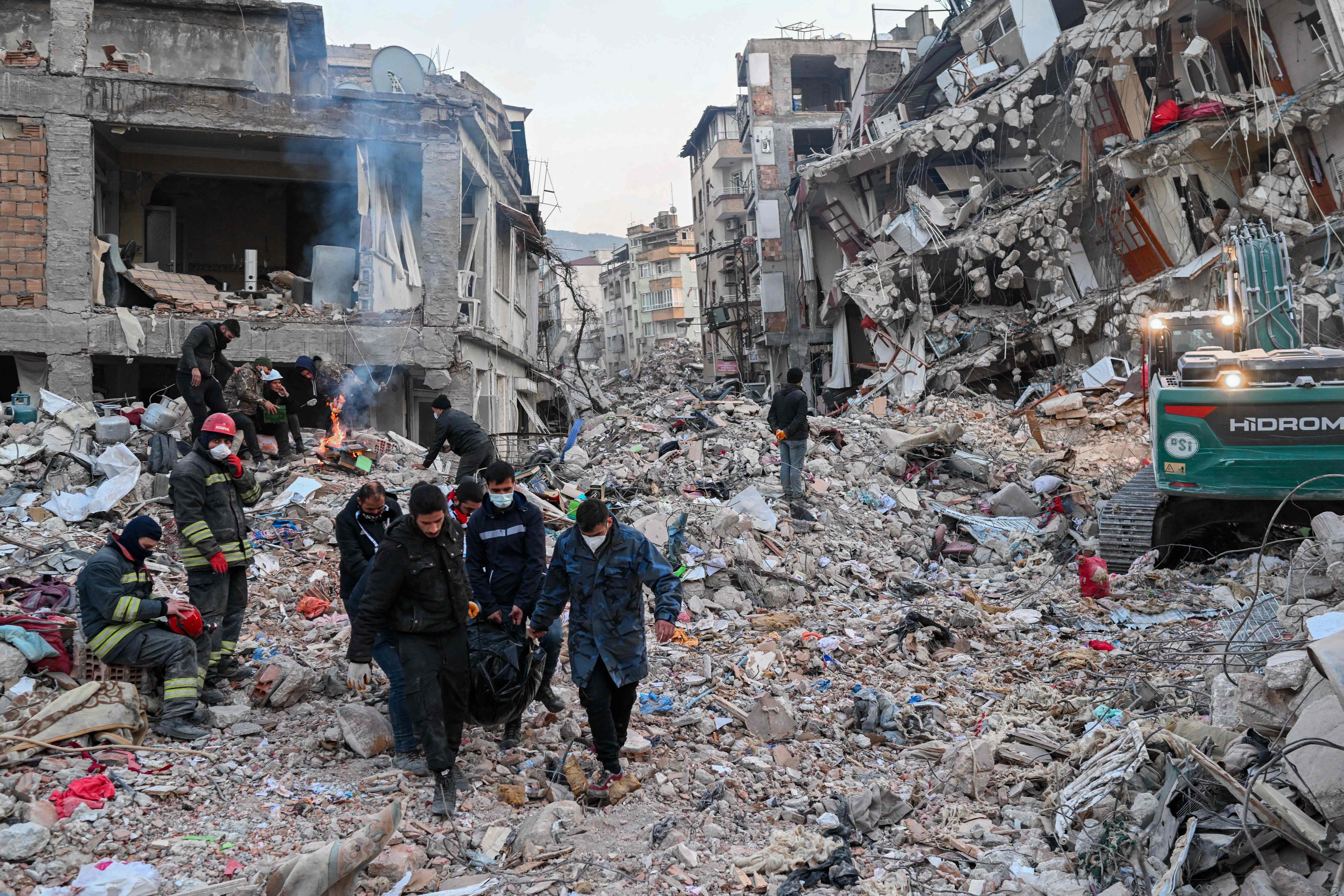 People carry a body bag as residents wait for their relatives to be pulled out from the rubble of collapsed buildings in Hatay