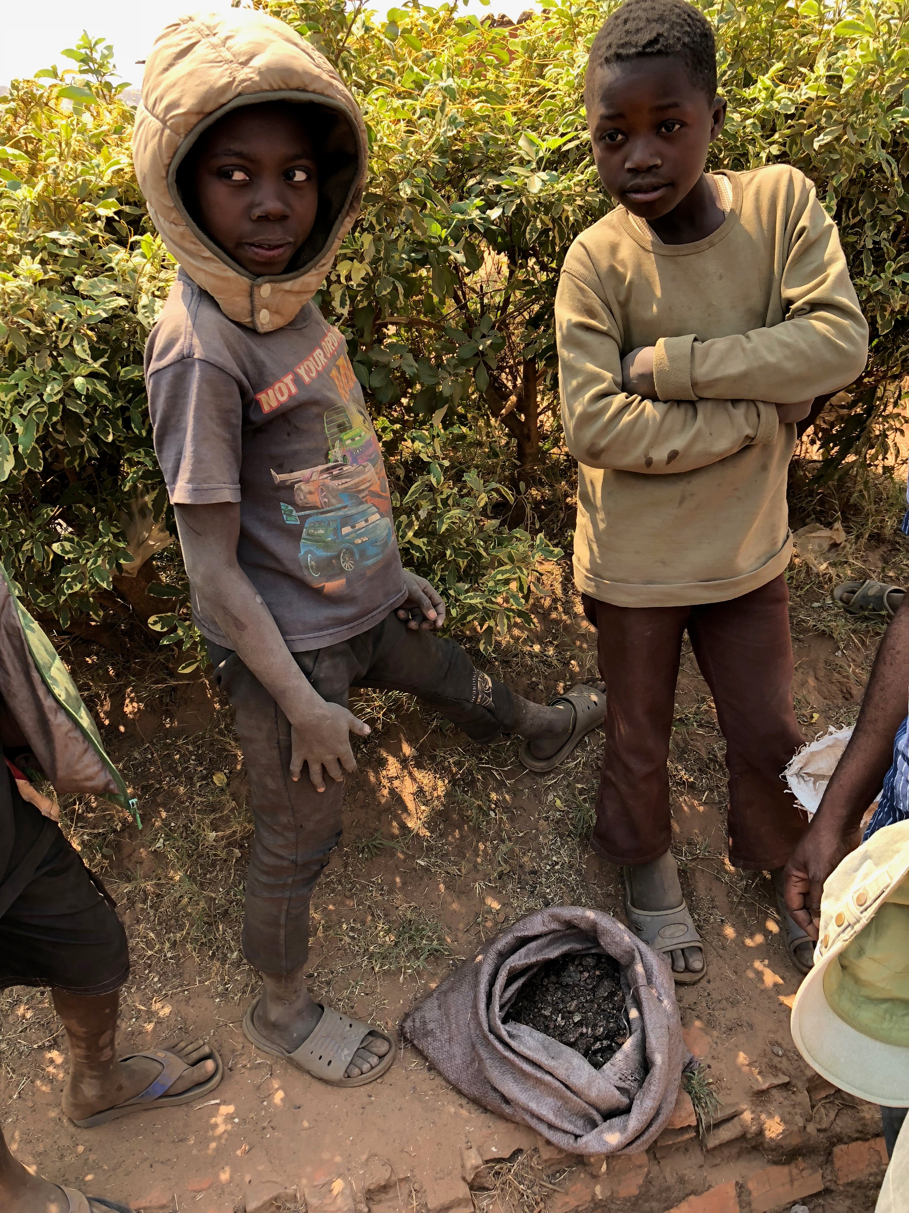 <p>Two boys stand over their sack of scraps of cobalt. Thousands of children are mining for cobalt in the DRC as their families cannot afford to pay school fees on meagre wages</p>