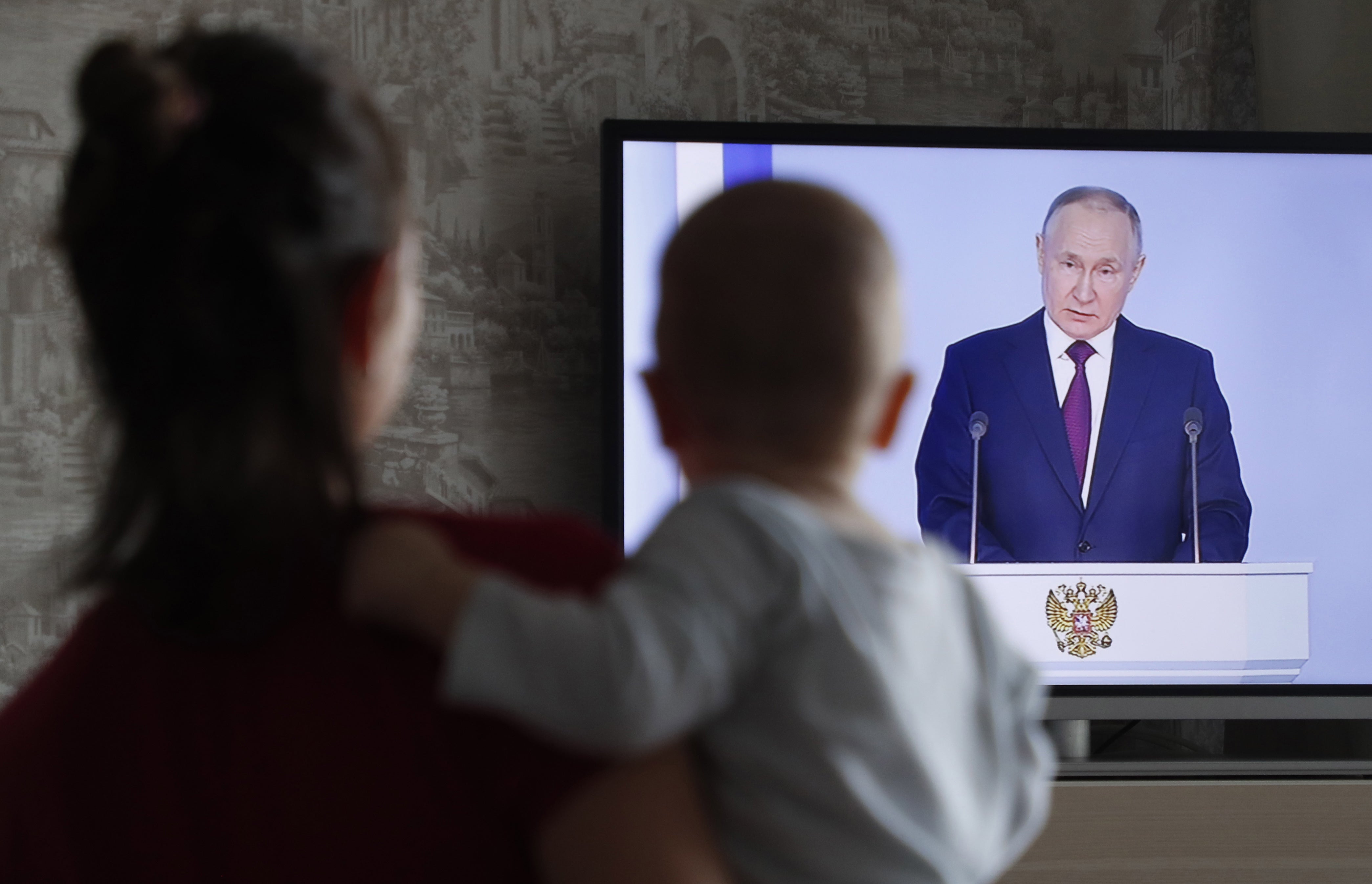 A woman holds her child as she watches the televised address by Russian president Vladimir Putin