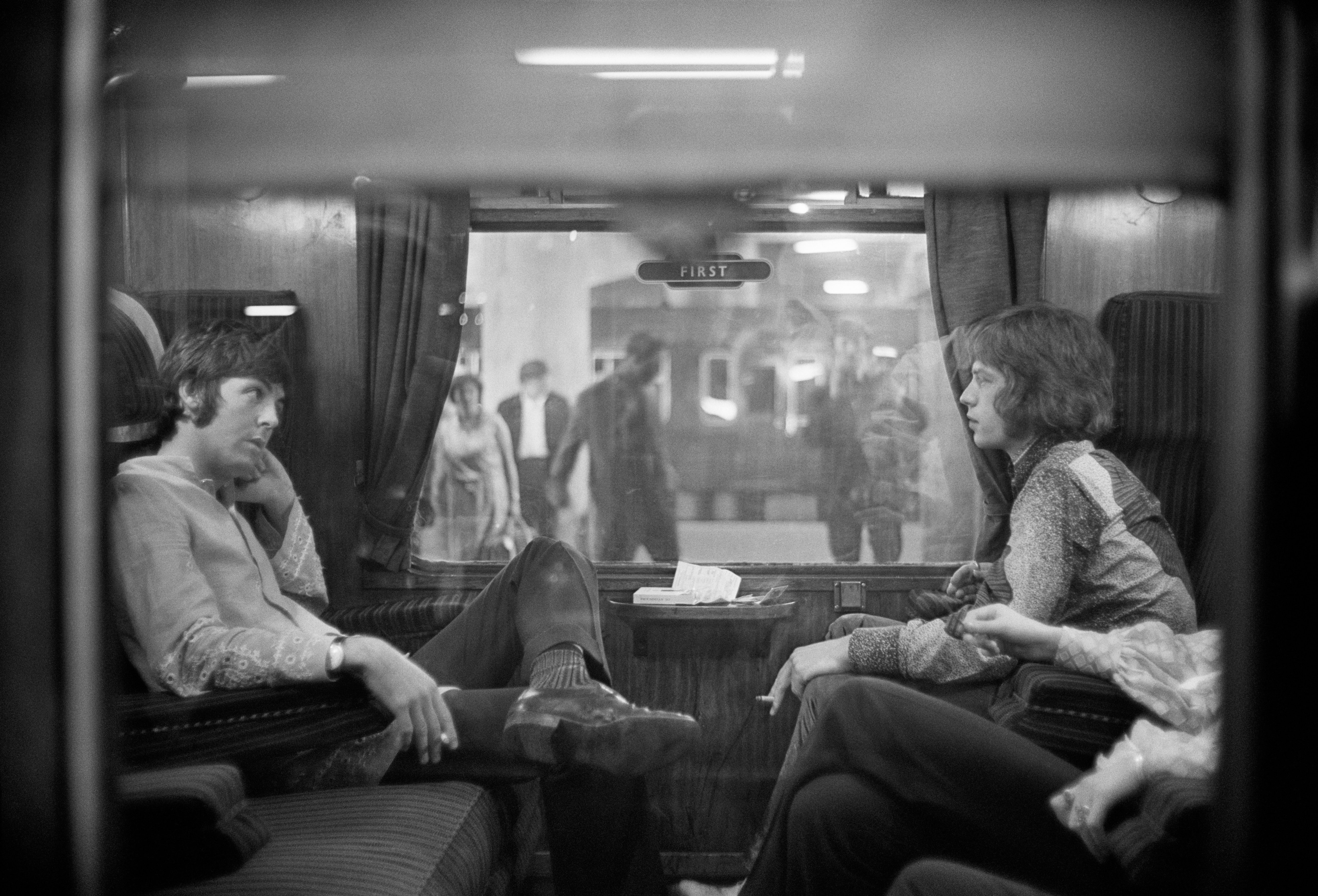 Paul McCartney of The Beatles and Mick Jagger of The Rolling Stones sit opposite each other on a train at Euston Station in 1967