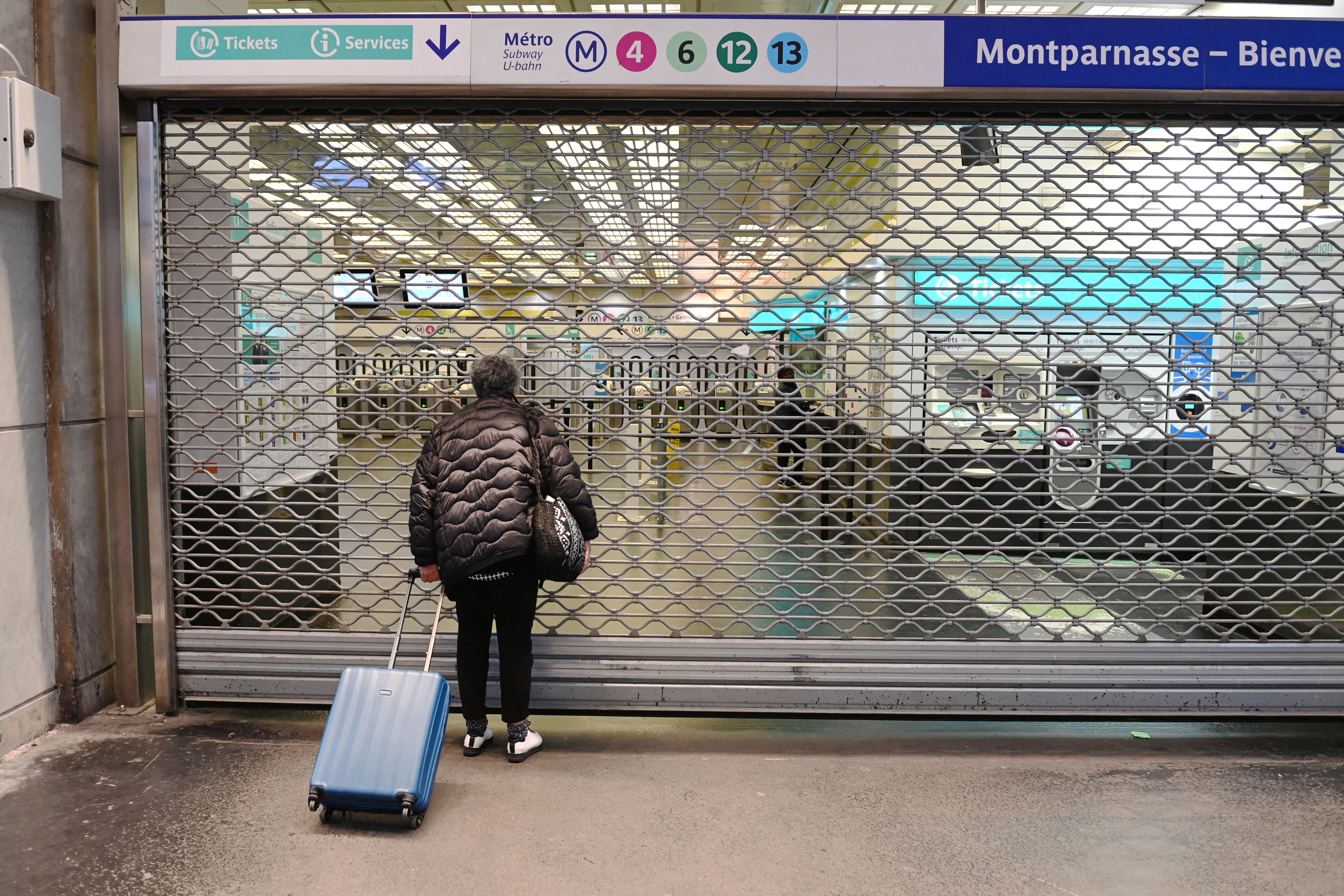 A passenger stands near the closed gate of the Montparnasse-Bienvenue Metro in Paris during industrial action