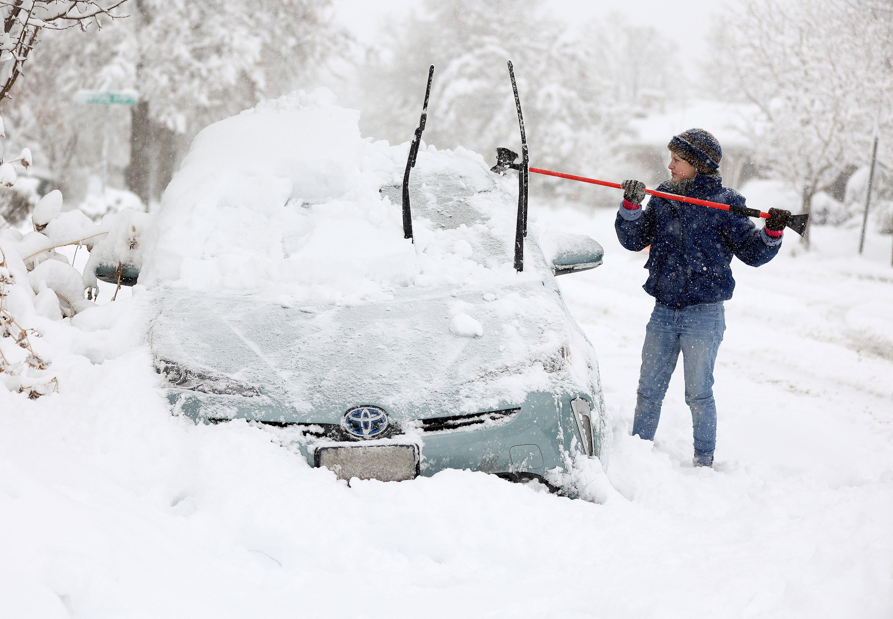 Cathy Morgan-Mace cleans snow and ice off her family's car during a snowstorm in Salt Lake City, Utah, on Wednesday