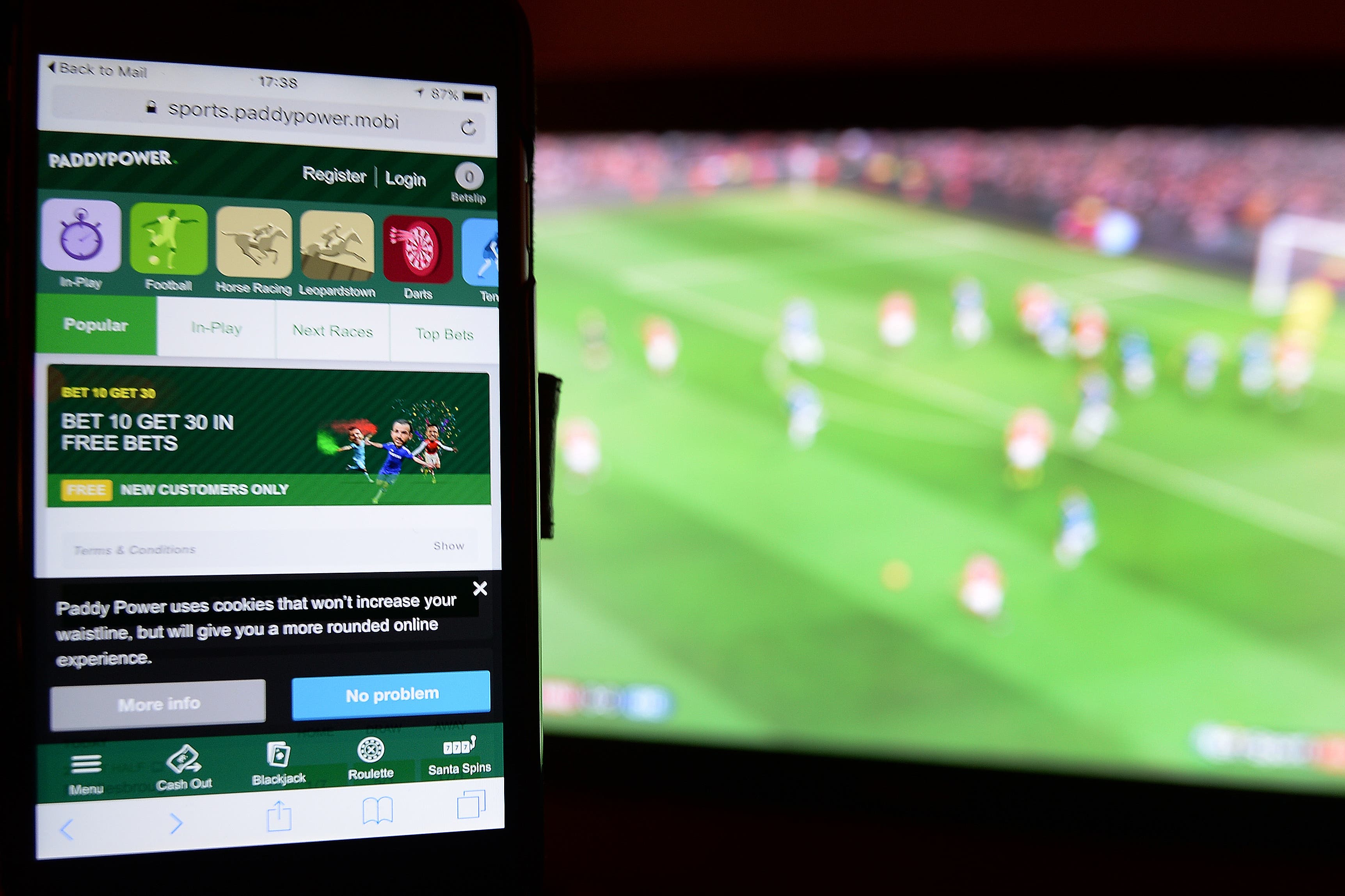 A smartphone user accesses a gambling website while watching a football match on television.