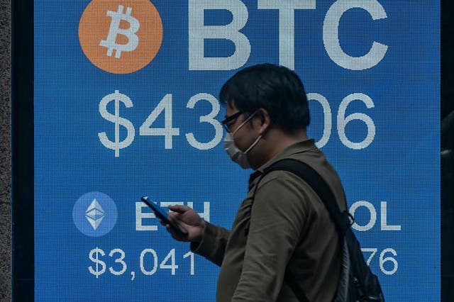 <p>A pedestrian walks past a digital screen displaying the prices of cryptocurrencies bitcoin on 15 February, 2022, in Hong Kong</p>
