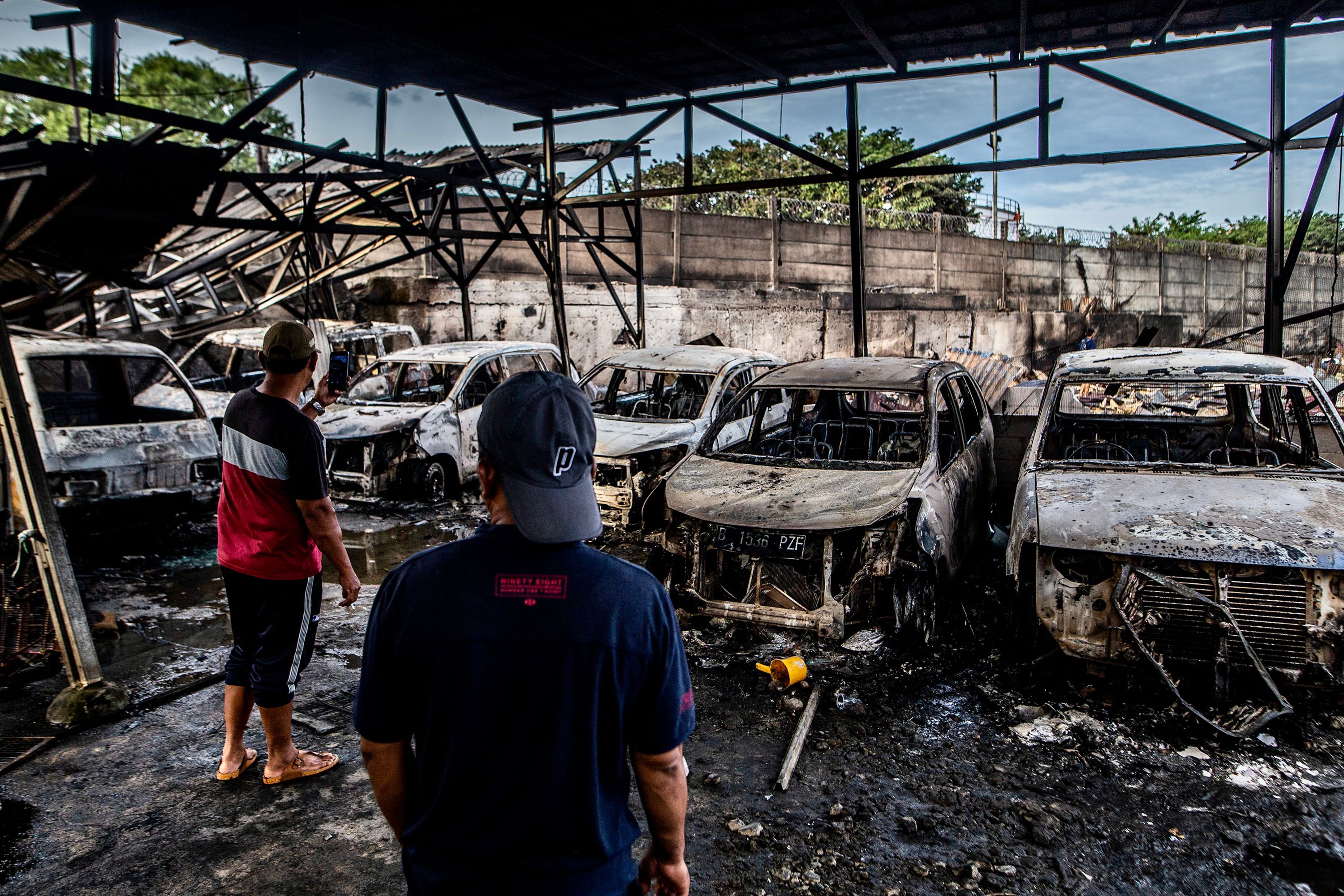 Two men look at burnt cars in Plumpang, north Jakarta on 4 March 2023, after a fire at a nearby state-run fuel storage depot run by energy firm Pertamina