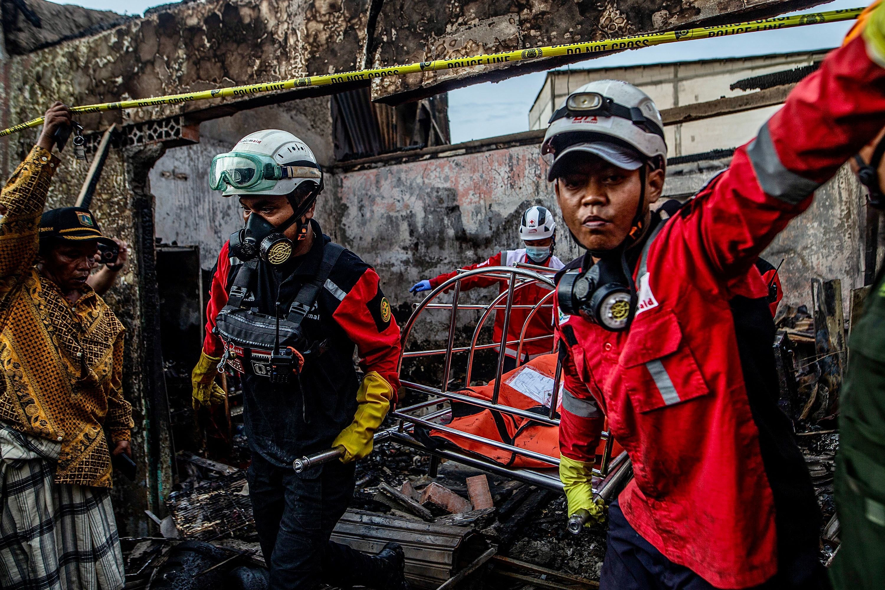 Firefighters evacuate a victim’s body from a house in a residential area in Plumpang, north Jakarta on 4 March 2023, after a fire at a nearby state-run fuel storage depot run by energy firm Pertamina