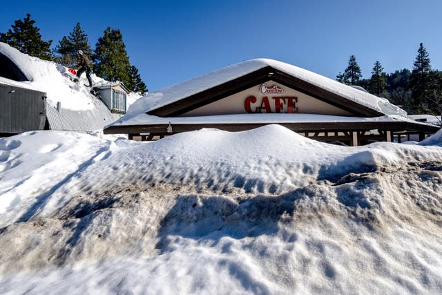 <p>A man shovels snow off the roof of a store in Crestline, California on Friday, 3 March, 2023, as buildings remain buried in several feet of snow from recent winter storms</p>