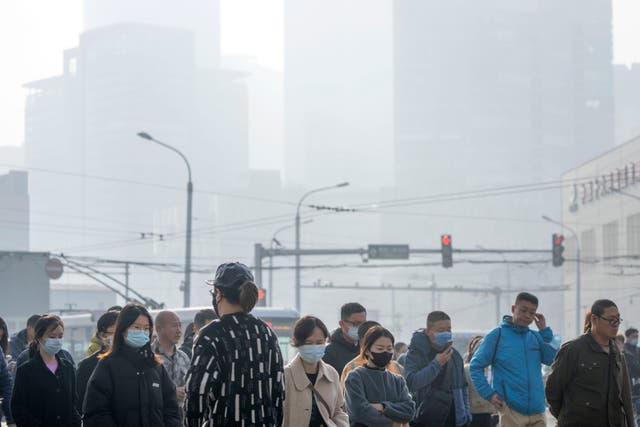 <p>Commuters wearing face masks walk across an intersection in the central business district on a day with high levels of air pollution in Beijing</p>