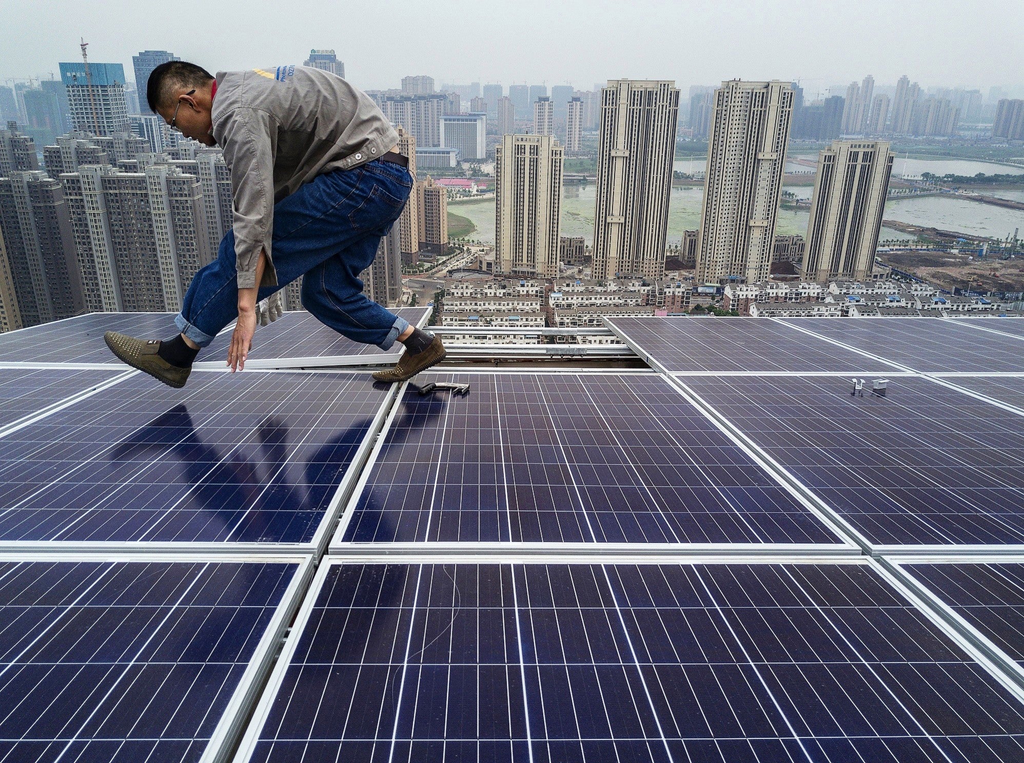 A Chinese worker installing solar panels on the roof of a 47 story building in Wuhan, China, on 15 May, 2017