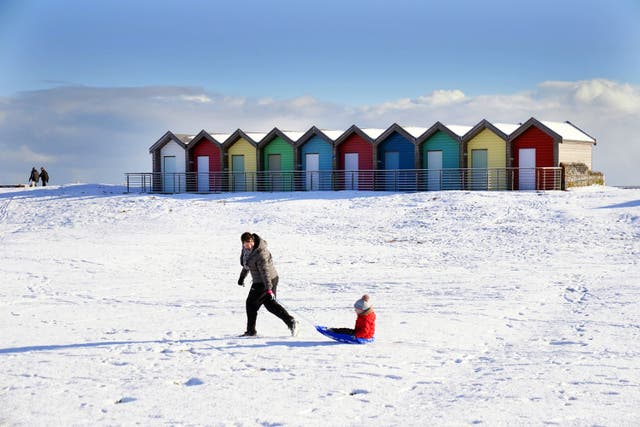 A woman pulls a child on a sledge through the snow beside the beach huts at Blyth in Northumberland (Owen Humphreys/PA)