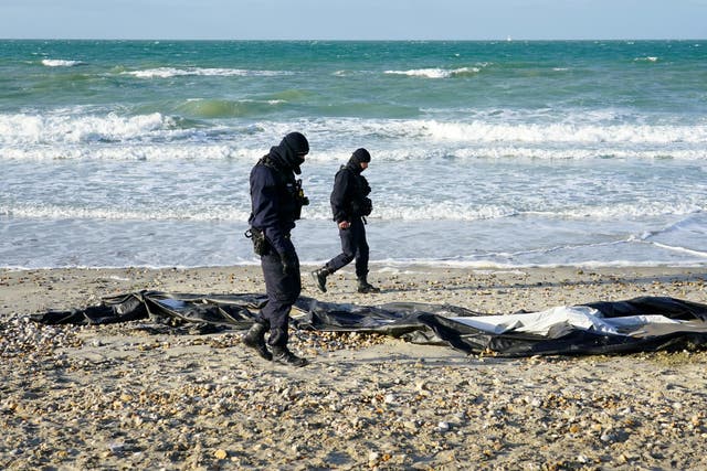 <p>French police officers pass a deflated dinghy on the beach in Wimereux near Calais (Gareth Fuller/PA)</p>