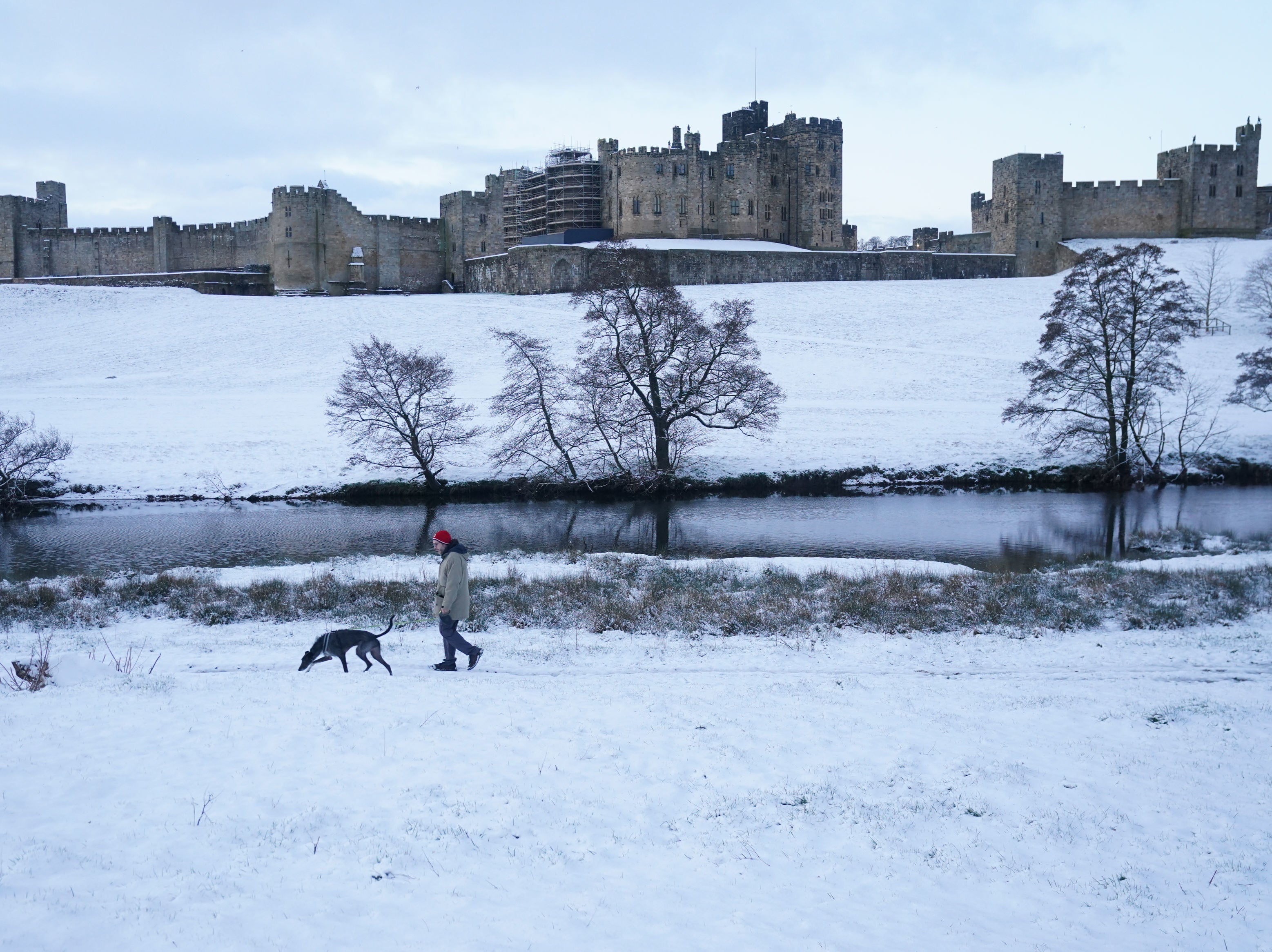 A man walks his dog through a snow covered field at Alnwick Castle in Northumberland