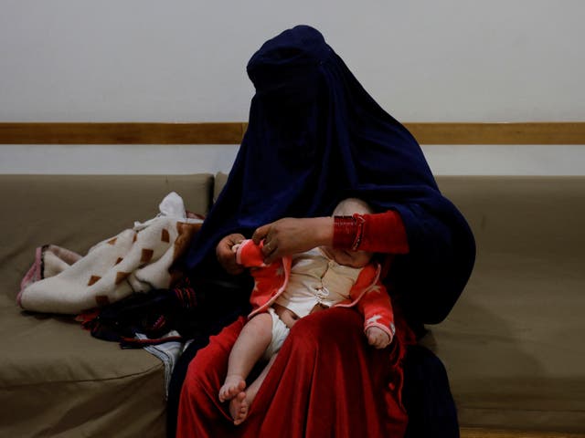 <p>A woman dresses up her child at a hospital in Bamiyan</p>