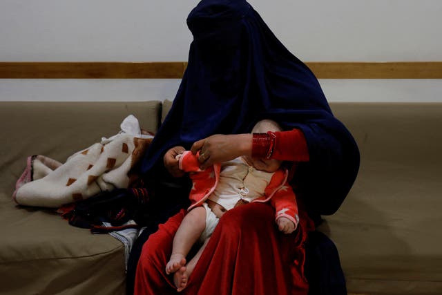 <p>A woman dresses up her child at a hospital in Bamiyan</p>