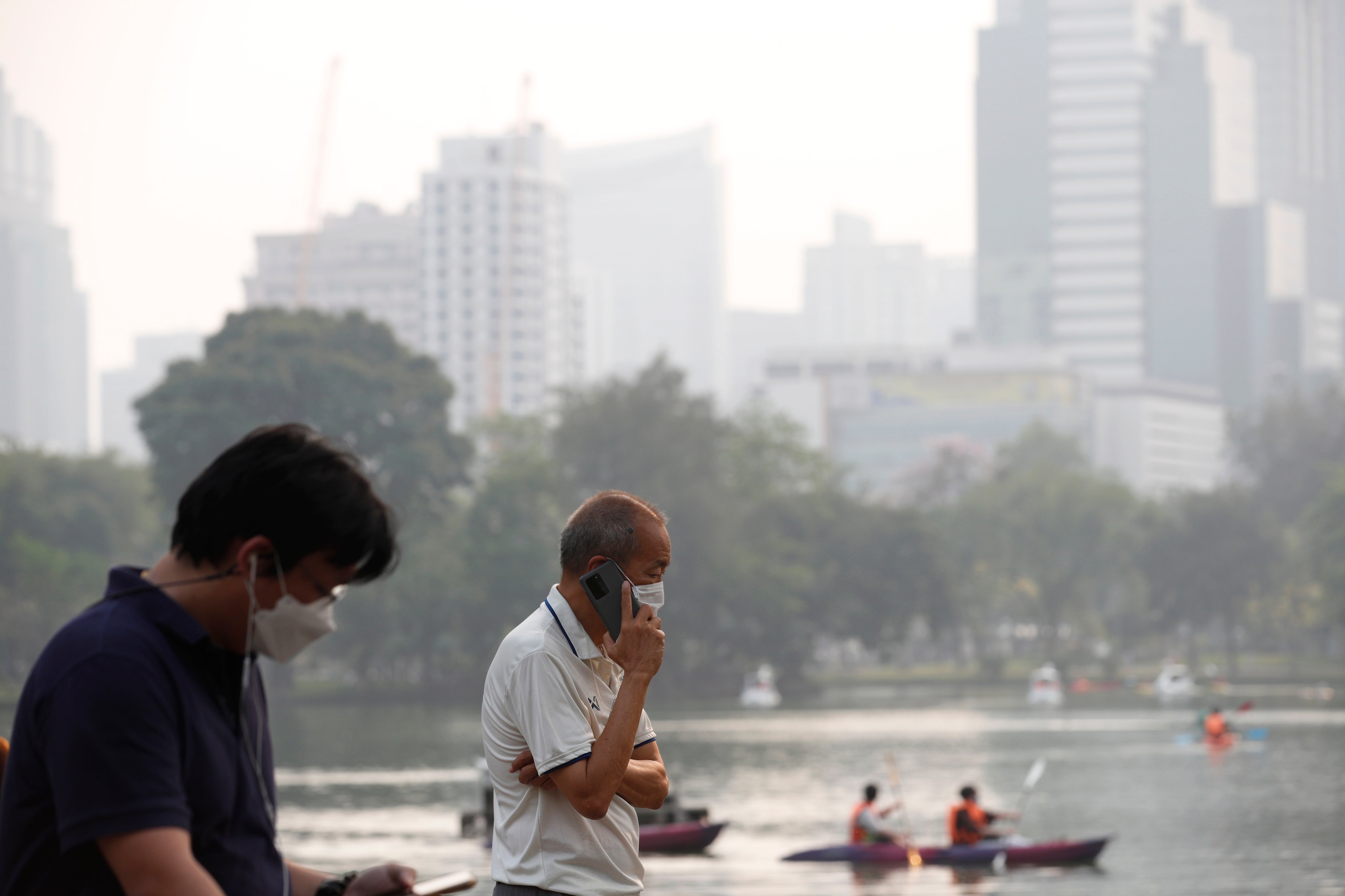 People wear face masks as high-rise buildings are shrouded in smog and haze from heavy fine dust at Lumpini Park in Bangkok