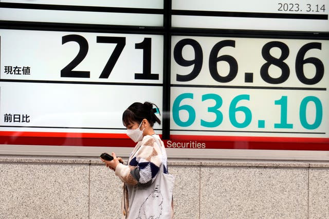 <p>File photo: A person wearing a protective mask walks past an electronic stock board showing Japan’s Nikkei 225 index</p>