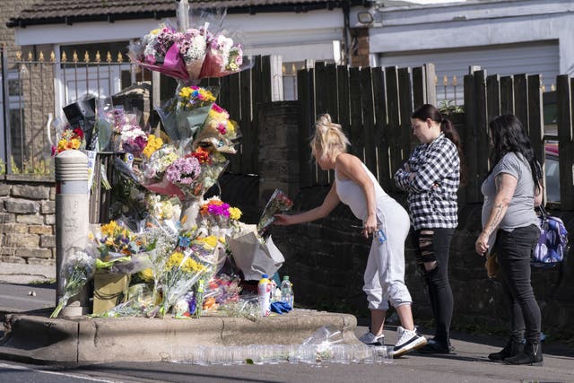 People lay a floral tributes at the scene in Woodhouse Hill, Huddersfield, where 15-year-old schoolboy Khayri McLean was fatally stabbed outside his school gates (PA)
