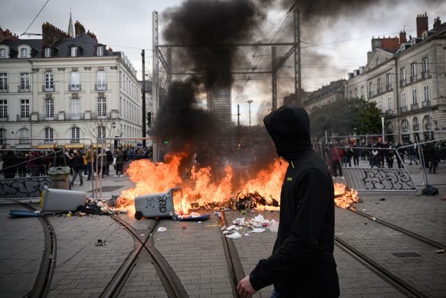 <p>A man passes a burning barricade following demonstrations in Nantes, western France, on 18 March 2023</p>