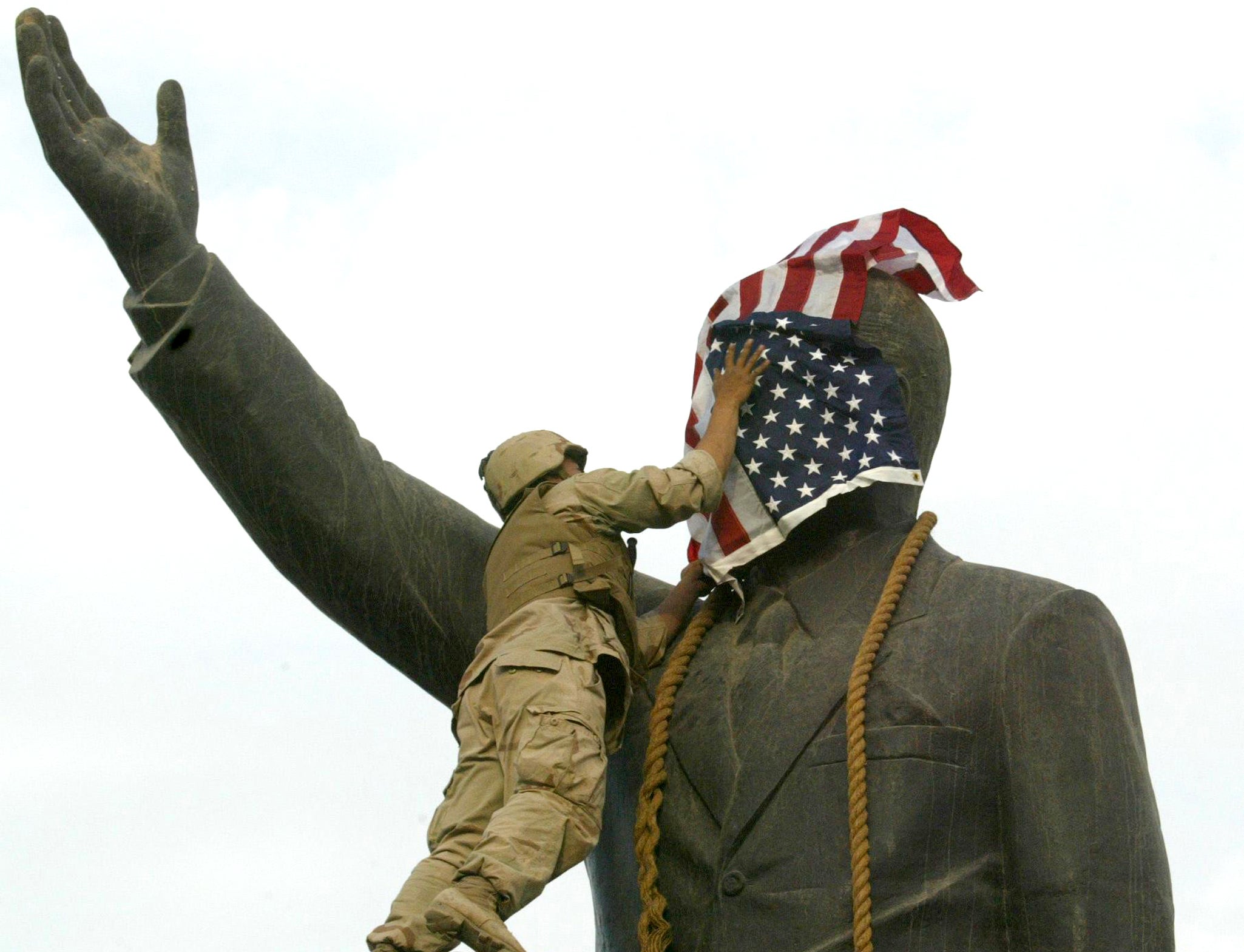 A US Marine drapes a flag over the face of Saddam Hussein