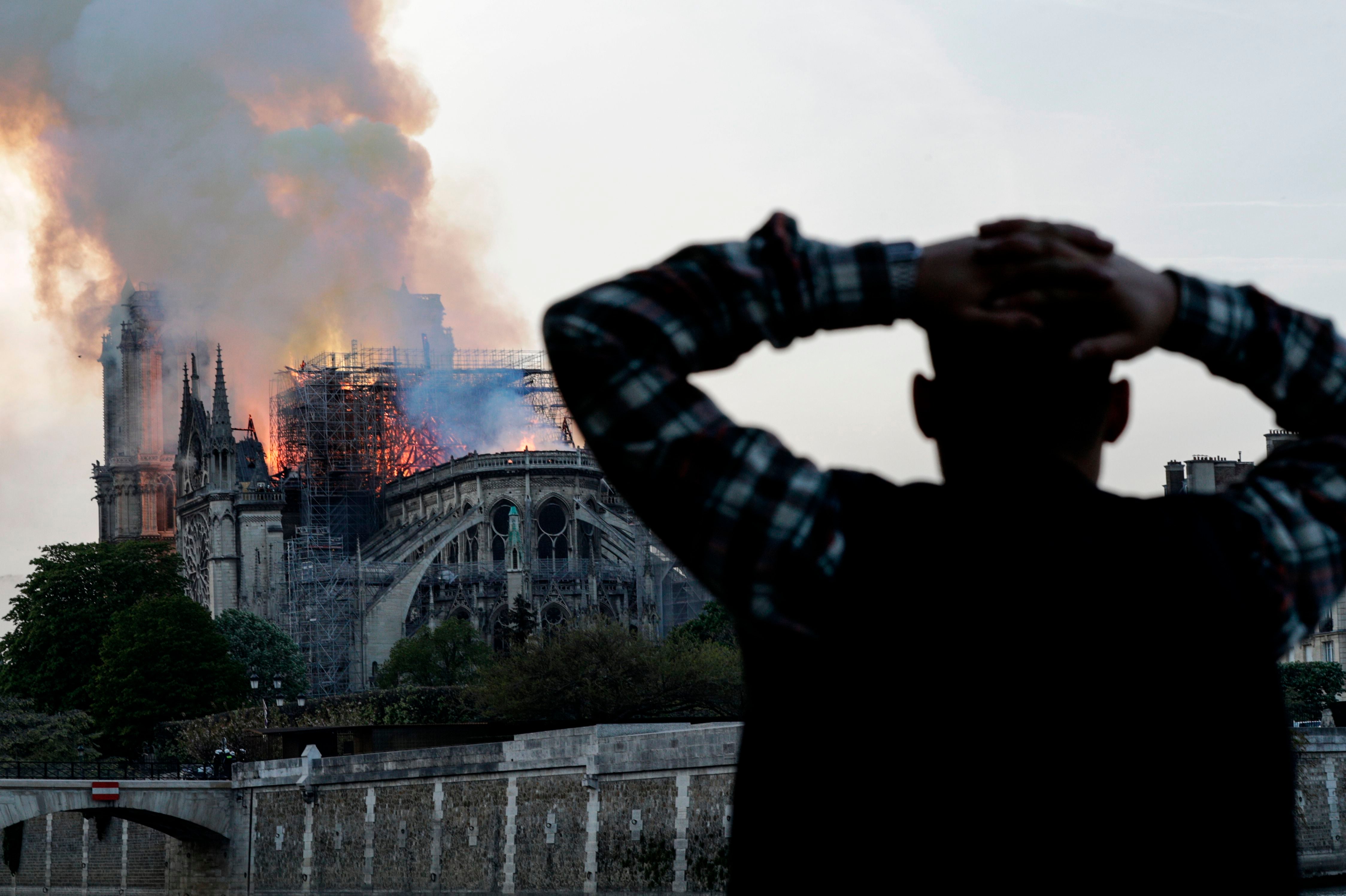 A bystander watches in despair as flames engulf the roof on 15 April 2019