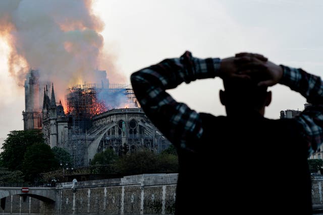 <p>A bystander watches in despair as flames engulf the roof on 15 April 2019 </p>