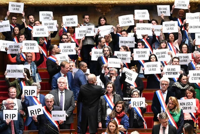 <p>Opposition MPs hold signs reading ‘64 is a no’ and ‘See you in the streets’ after narrowly losing a no-confidence vote over pension reforms</p>