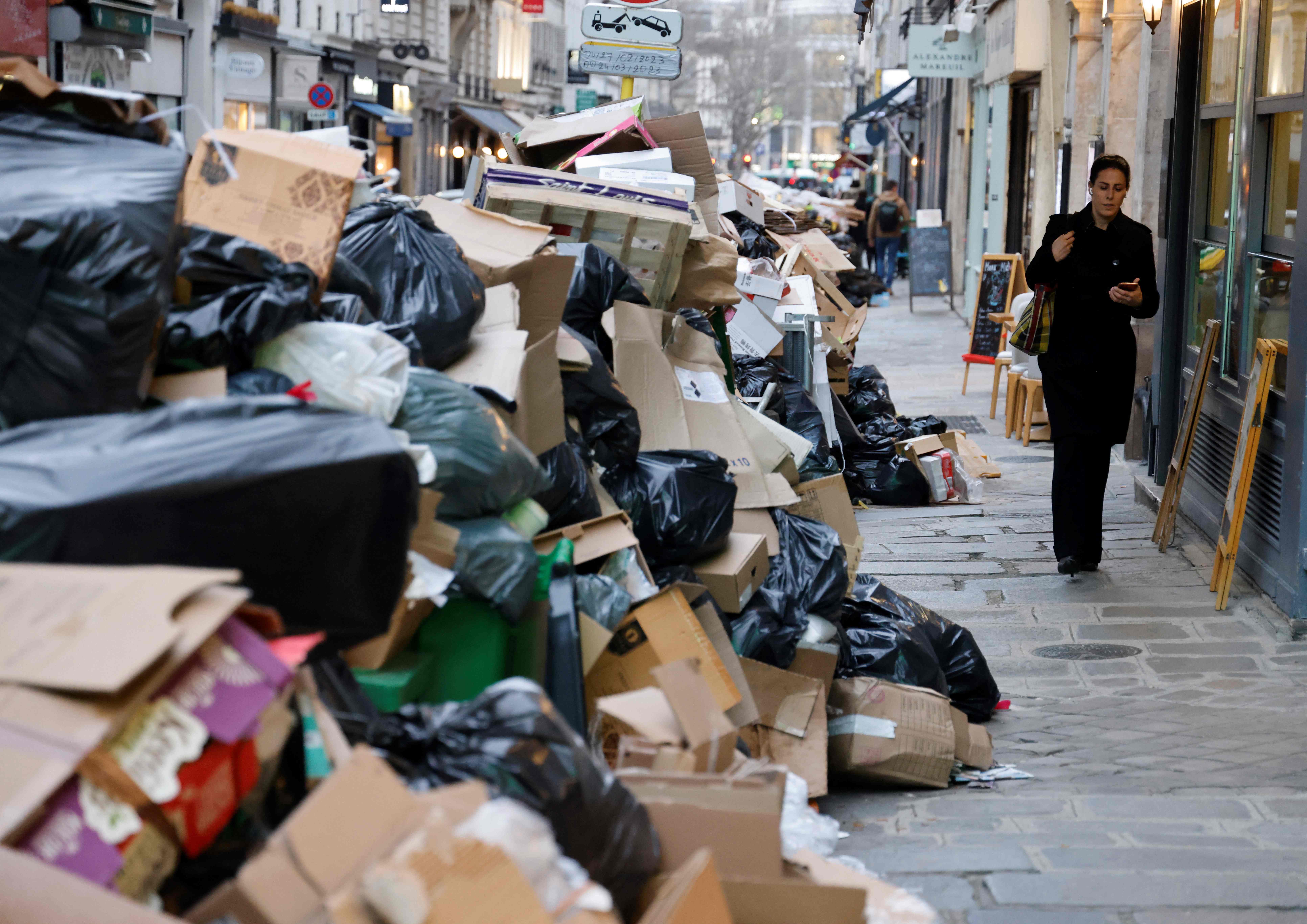 A woman walks past a pile of uncollected rubbish in Paris as strikes entered their 15th day