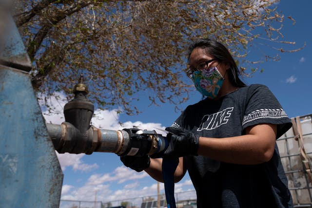 <p>Raynelle Hoskie attaches a hose to a water pump to fill tanks in her truck outside a tribal office on the Navajo reservation in Tuba City, Ariz., on April 20, 2020</p>