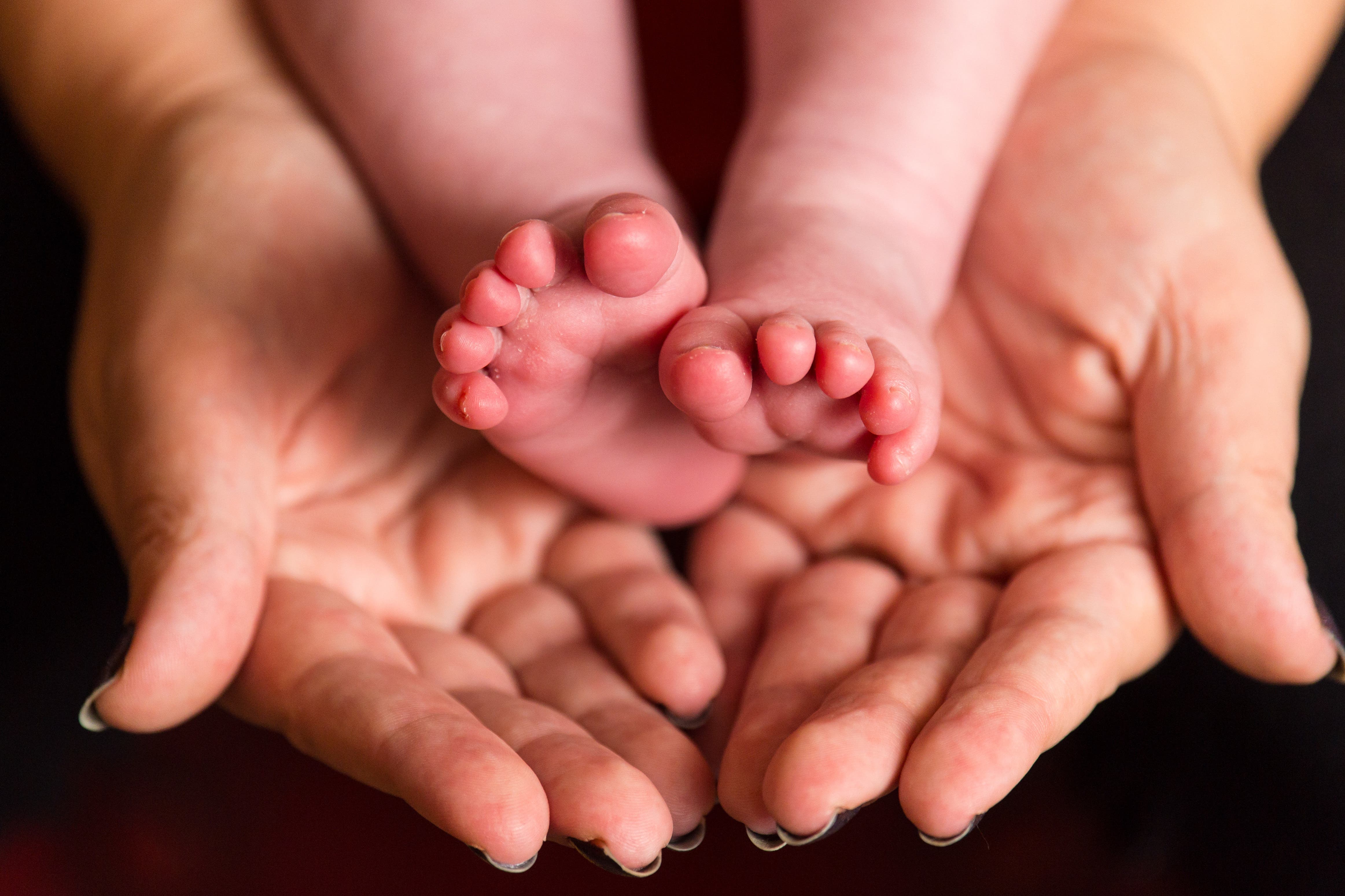 A mother holds the feet of a new baby (Dominic Lipinski/PA)