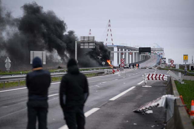 <p>Protestors look on next to a damaged and burning road sign gantry at the entrance of the "Pont de Saint-Nazaire" (Saint-Nazaire bridge), the longest bridge in France</p>