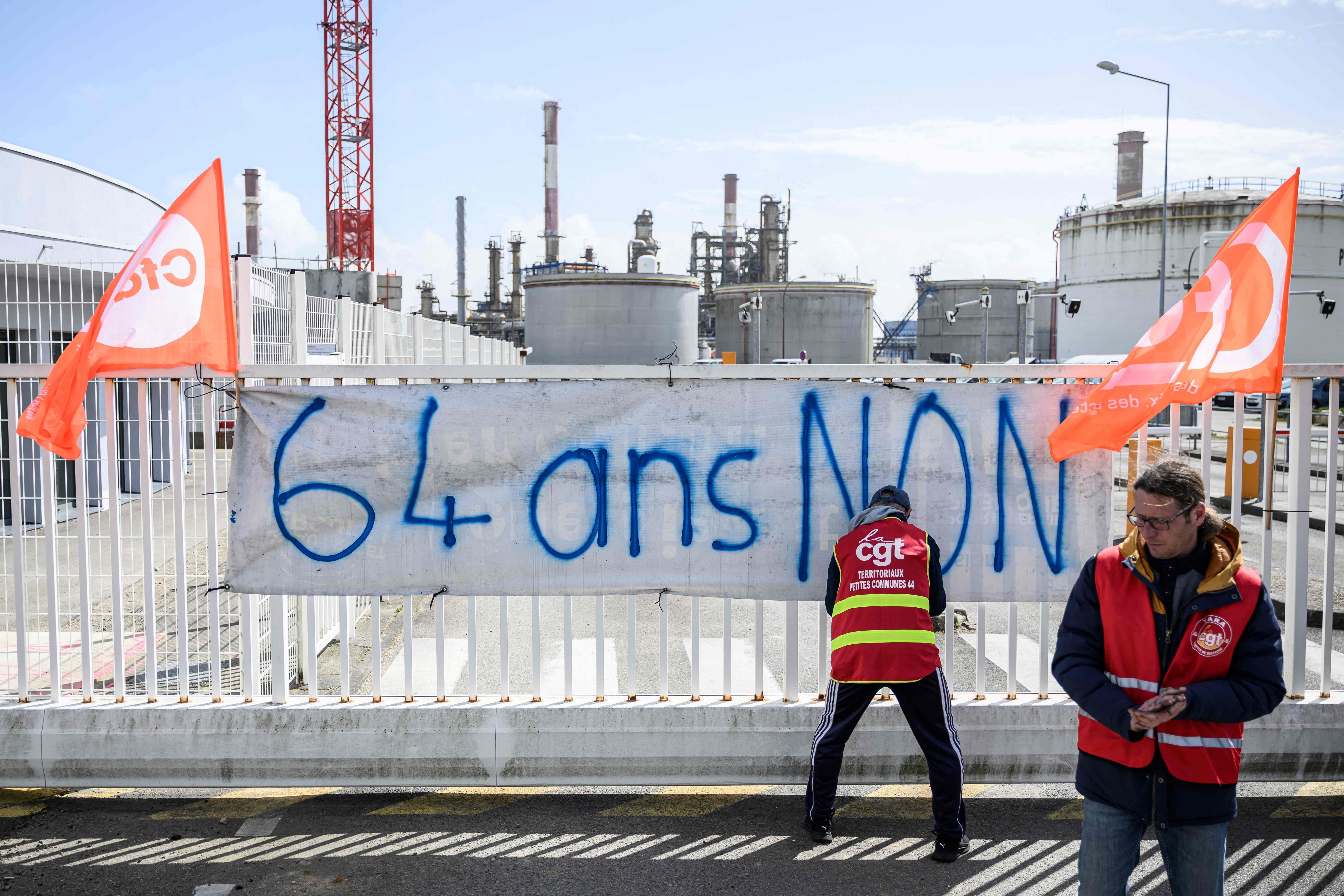 TotalEnergie workers and union members attach a banner reading "64-years-old, No" as they block the entrance of the Donges refinery