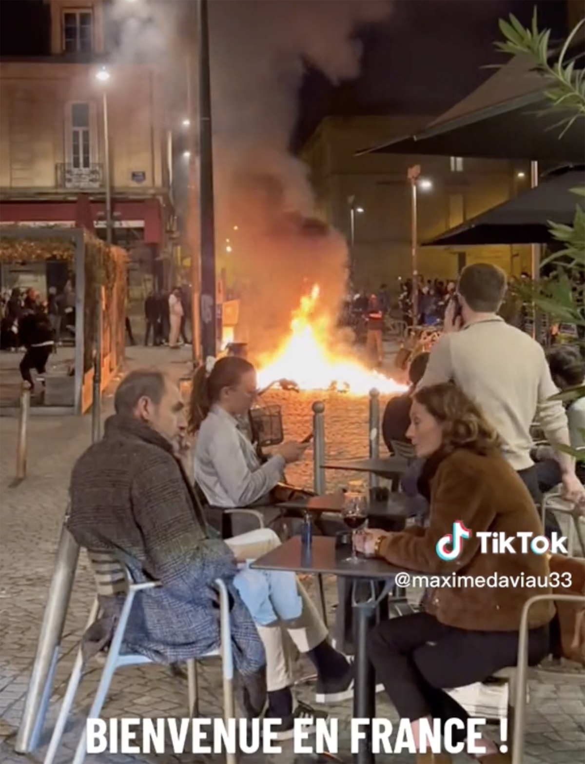 French diners enjoy glass of wine as city burns in background