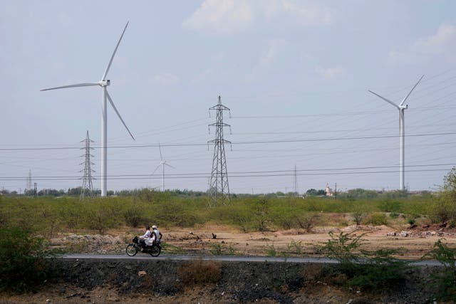 <p>A motorcyclist ride past wind turbines near Sadla village in Surendranagar district of Gujarat state, India</p>