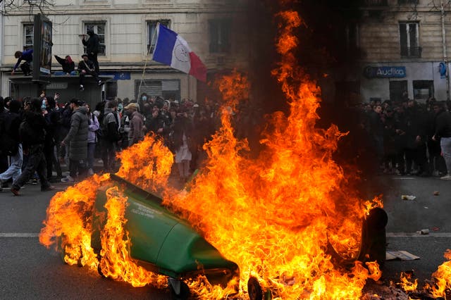 <p>Demonstrators walk past burning rubbish bins on 28 March, 2023 in Paris</p>