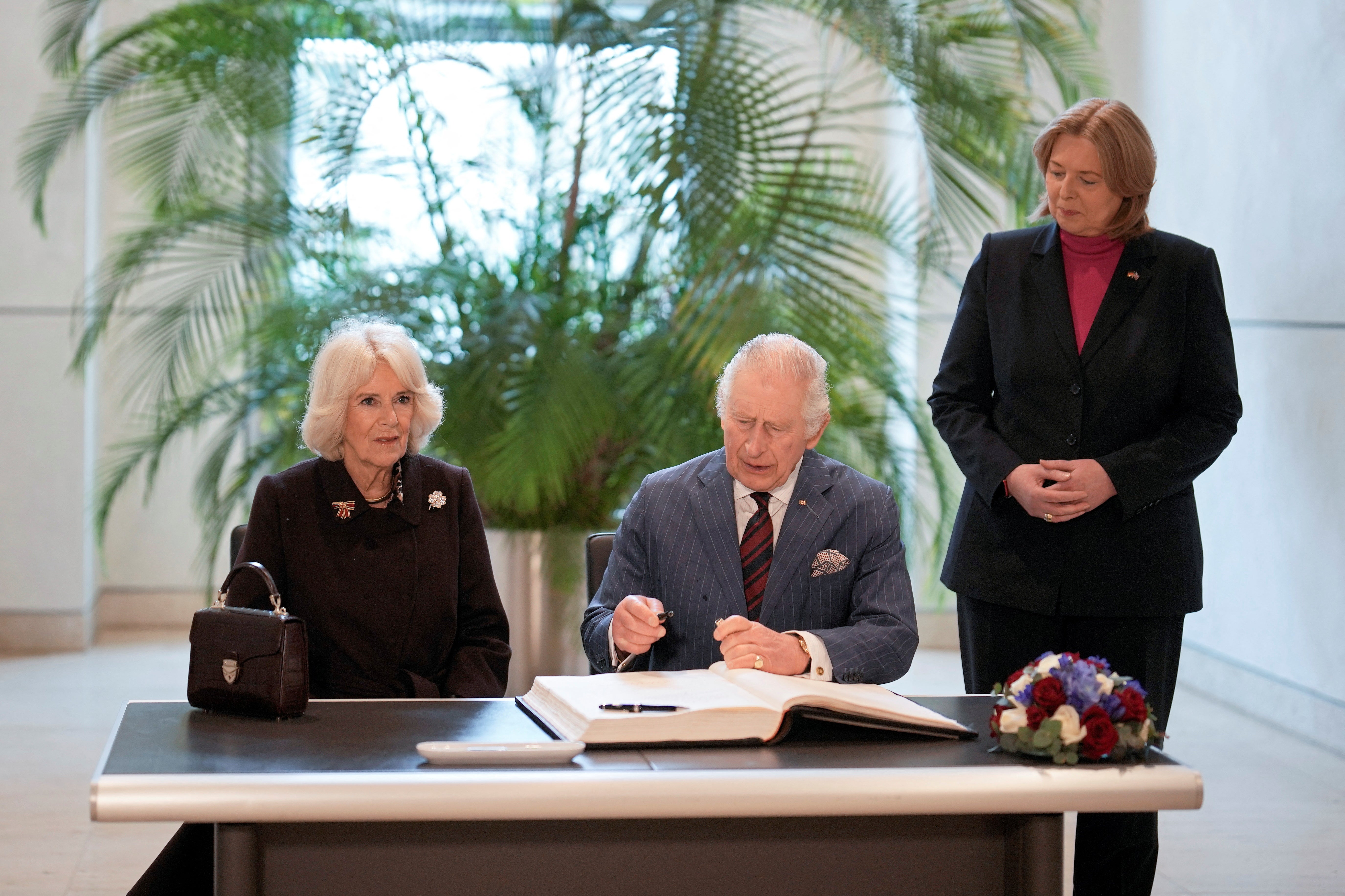 King Charles and Camilla, the Queen Consort, sign a guest book at the Bundestag, as German Bundestag President Baerbel Bas watches